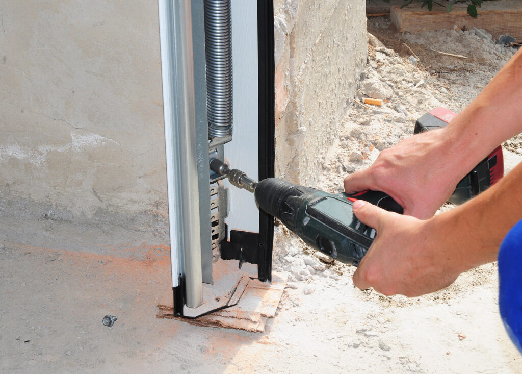 person using drill to insert screws on the bottom of a garage door